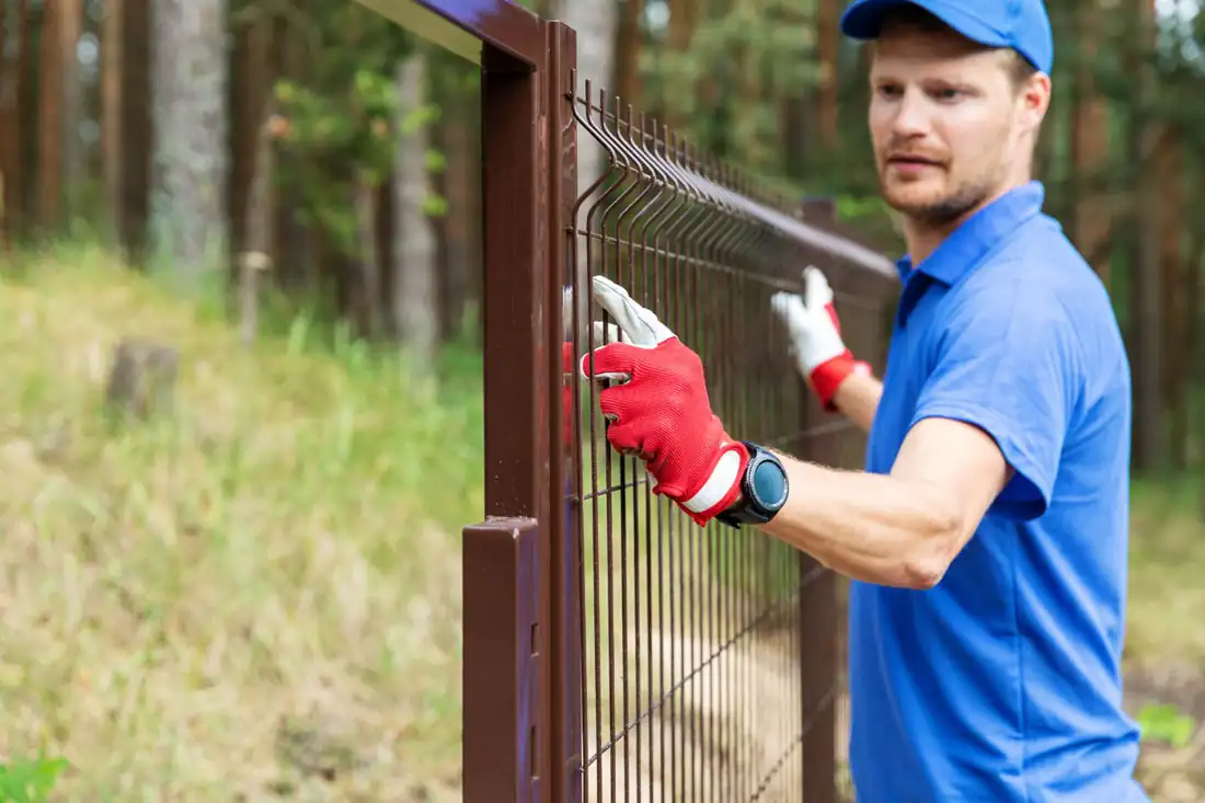 Installer attaching a metal fence panel to a post