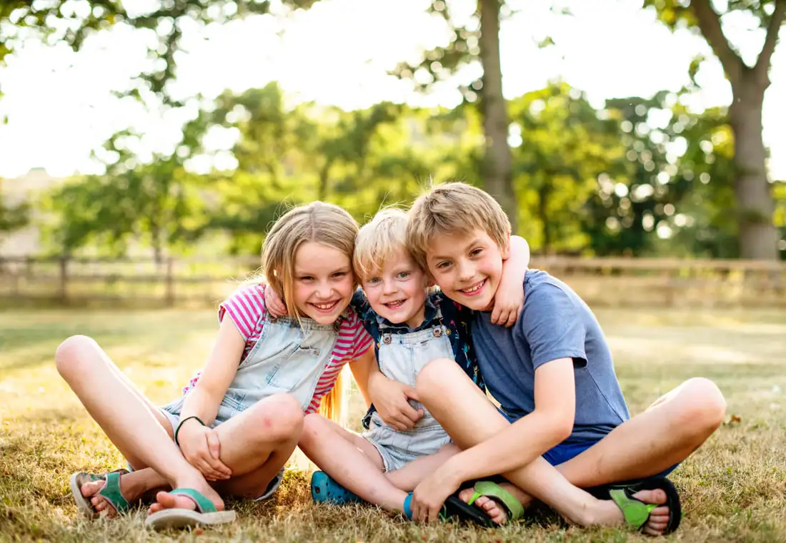 Children playing on a lawn beside a wooden split rail fence