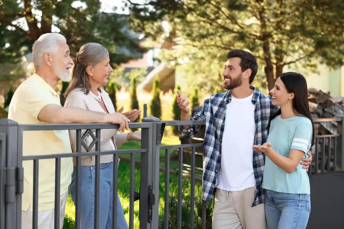 Two neighbors talking over a black aluminum fence