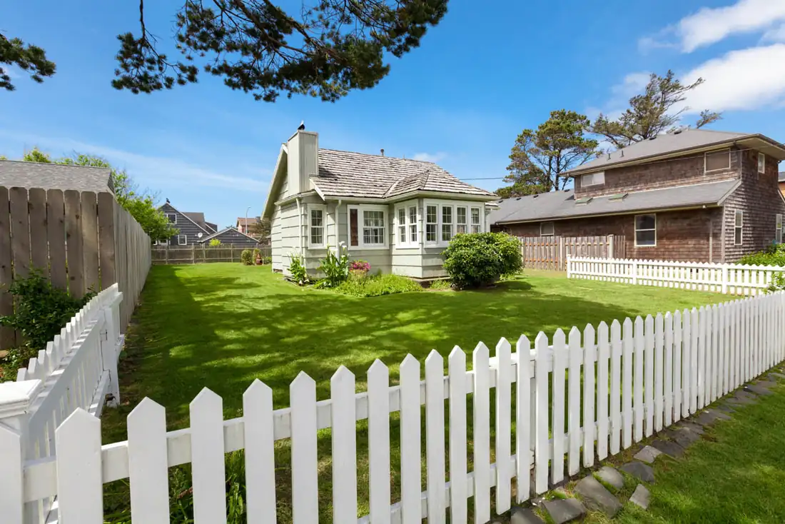White picket fence in front of a cottage-style home with a garden